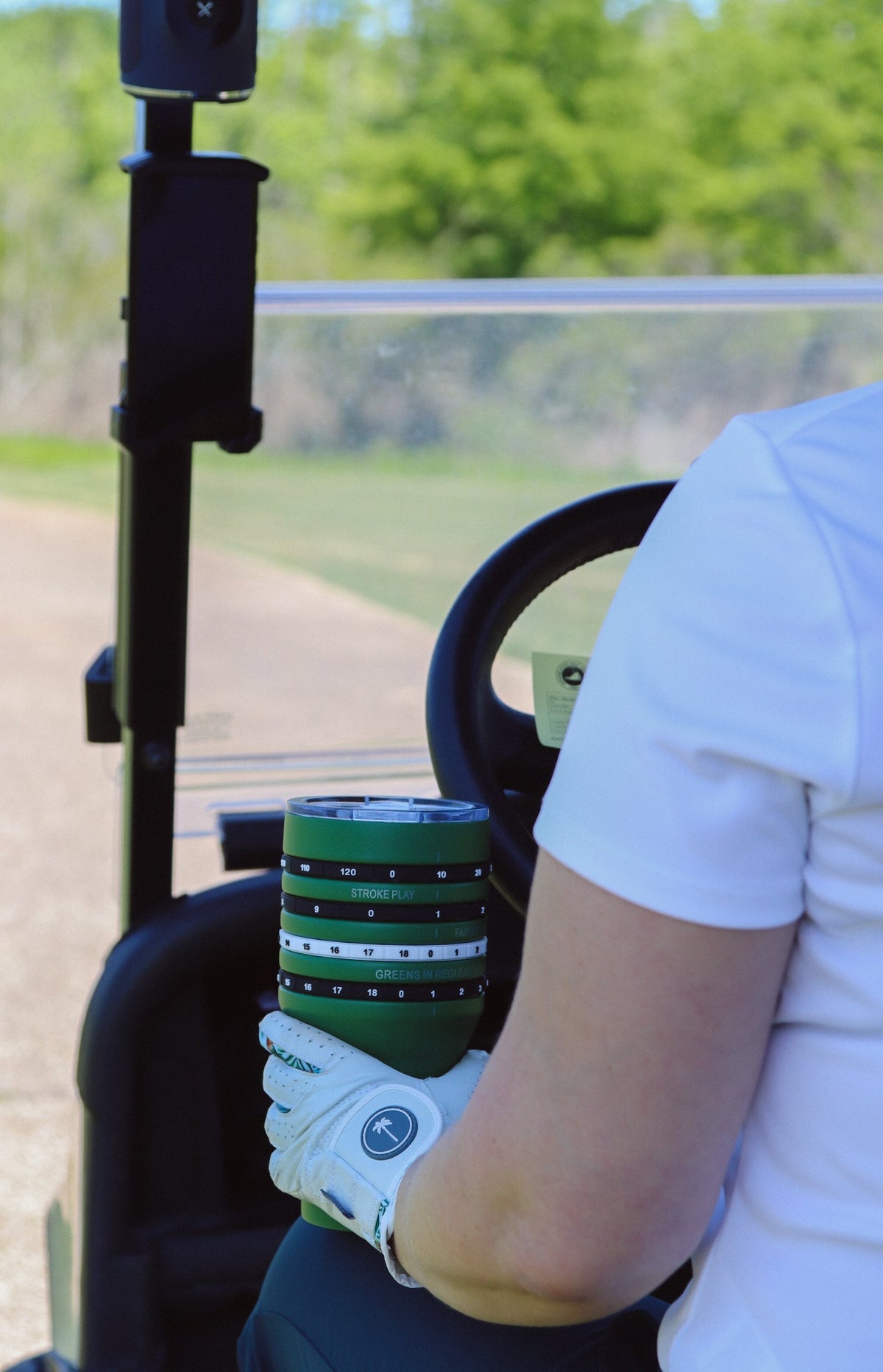 Person holding a tally tumbler and driving golf cart 
