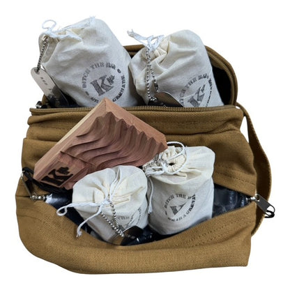 A tan canvas shoulder bag shown open, filled with several small off-white drawstring pouches printed with a circular logo and a wooden folding tray, photographed on a plain white background.