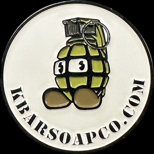 A round metal challenge coin with a design that includes a stylized grenade and the text 'KBARSOAPCO.COM'.