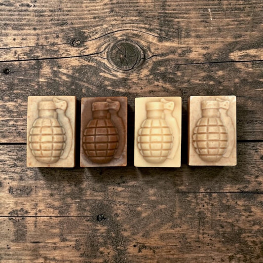 Four rectangular blocks, each containing an embossed grenade design, arranged in a row on a rustic dark wood background. The blocks show four different tones: light beige, medium brown, pale cream, and dark brown.