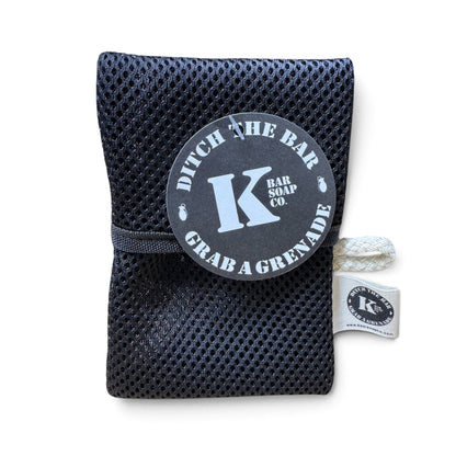 A black mesh bath sponge pouch with a gray circular tag reading 'Ditch the Bar Bar Soap Co. Grab a Grenade' and a white rope handle, shown on a white background.