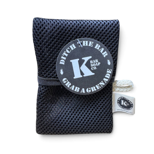 A black mesh bath sponge pouch with a gray circular tag reading 'Ditch the Bar Bar Soap Co. Grab a Grenade' and a white rope handle, shown on a white background.