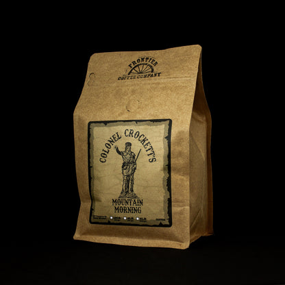 A paper bag packaging for Col. Crockett's Medium Roast coffee with a printed label featuring an illustration of a male figure and the name of the coffee variety.