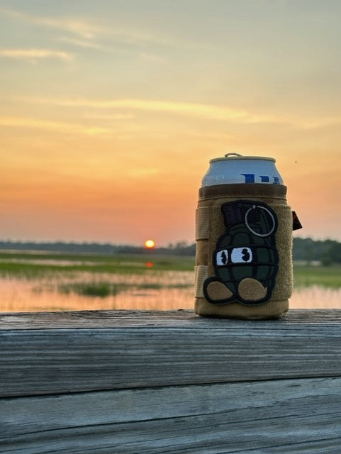 A beige koozie with design is displayed against a sunset backdrop.