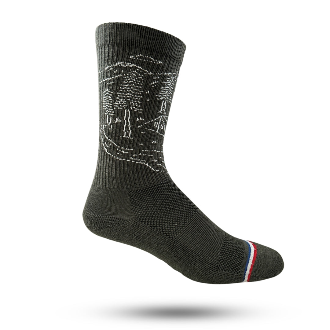 A pair of olive adventure socks with a cushioned sole and a reinforced heel and toe seam, featuring a striped design with red, white, and blue.