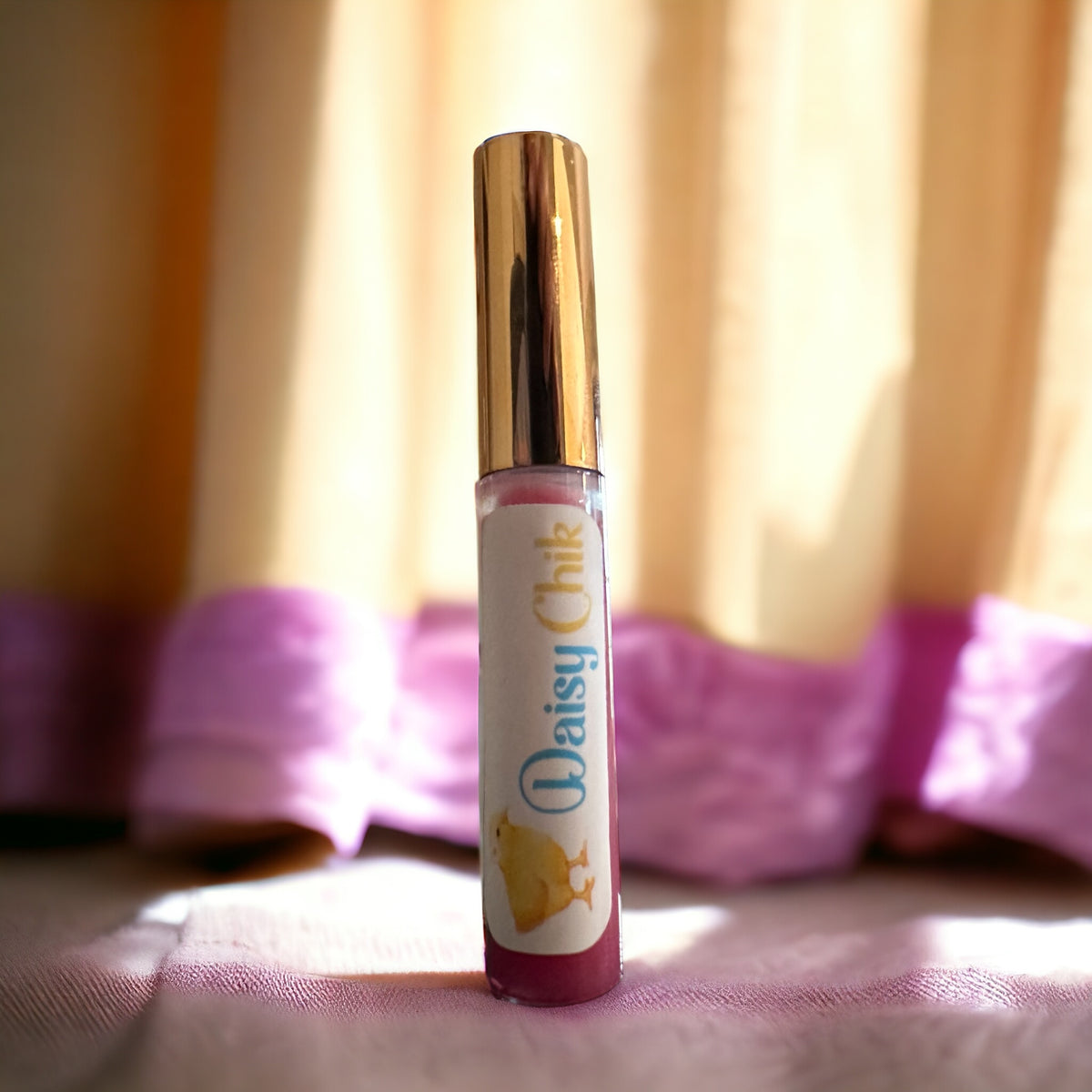 Daisy Chik natural lip gloss tube with gold cap by a window