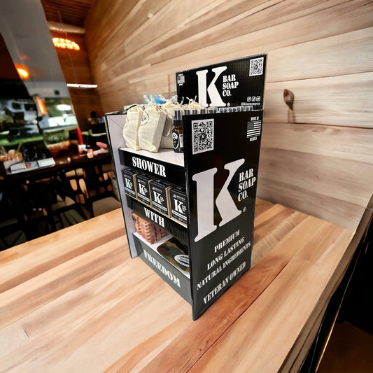 A retail display box with the branding 'K Bar Soap Co' on it, standing upright on a wooden surface, showcasing an example of a product setup within it.