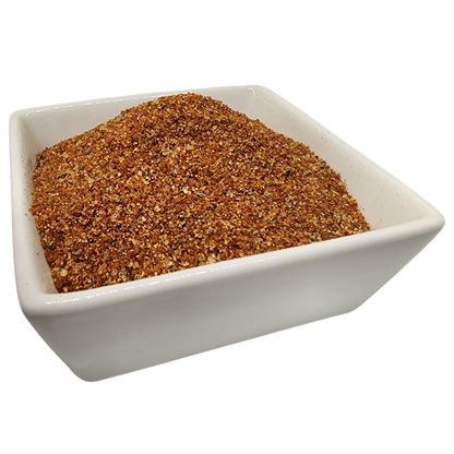 A mound of coarse brown spice or seasoning blend in a white square ceramic bowl, isolated on a white background.