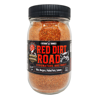 A jar of B's Red Dirt Road Signature BBQ Rub, containing a reddish-brown spice blend, with a black ribbed lid and a black label featuring red and white text.