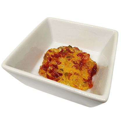 A small square white ceramic dish containing a glossy, translucent orange-red food mixture with visible red flecks, photographed on a plain white background.