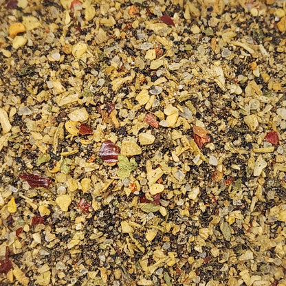 A close-up, top-down view of a textured spice blend containing ground black pepper, dried herbs, garlic, and red chili flakes.