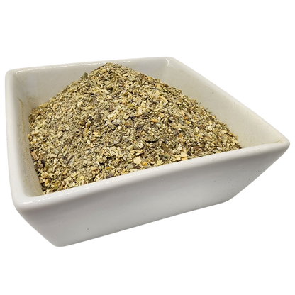 A mound of finely ground dried herbs or spices in beige and olive-green tones, presented in a small square white ceramic bowl against a plain white background.