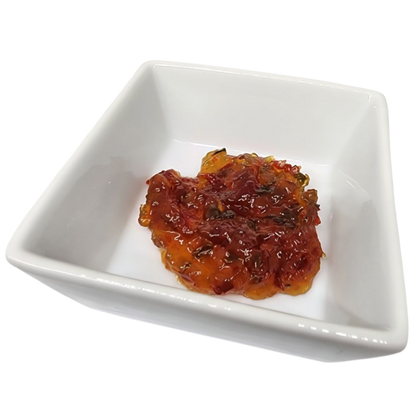 A small mound of glossy red-orange fruit spread or jam with visible dark fruit pieces, served in a white square ceramic dish on a white background.