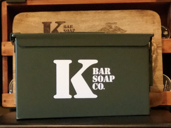 
                  
                    .50 Cal Ammo Can with K Bar Logo and Wood Cutting Board behind it
                  
                